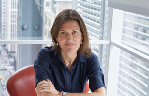 Kate Zernike sits at a table in front of window, with skyscrapers seen behind.