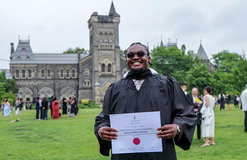 Jason Okpere poses for the camera in a grad gown, holding his diploma
