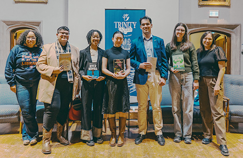 A group of people pose in Seeley hall with a Trinity Reads poster in the background